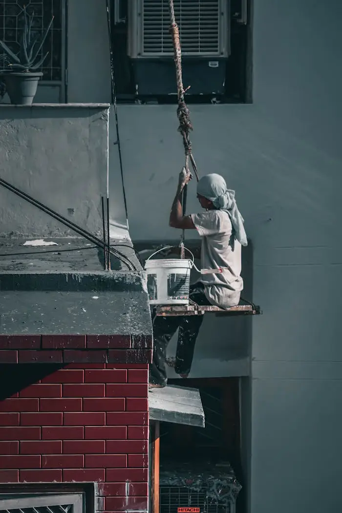 Worker on a scaffold painting a building exterior in New Delhi, India.