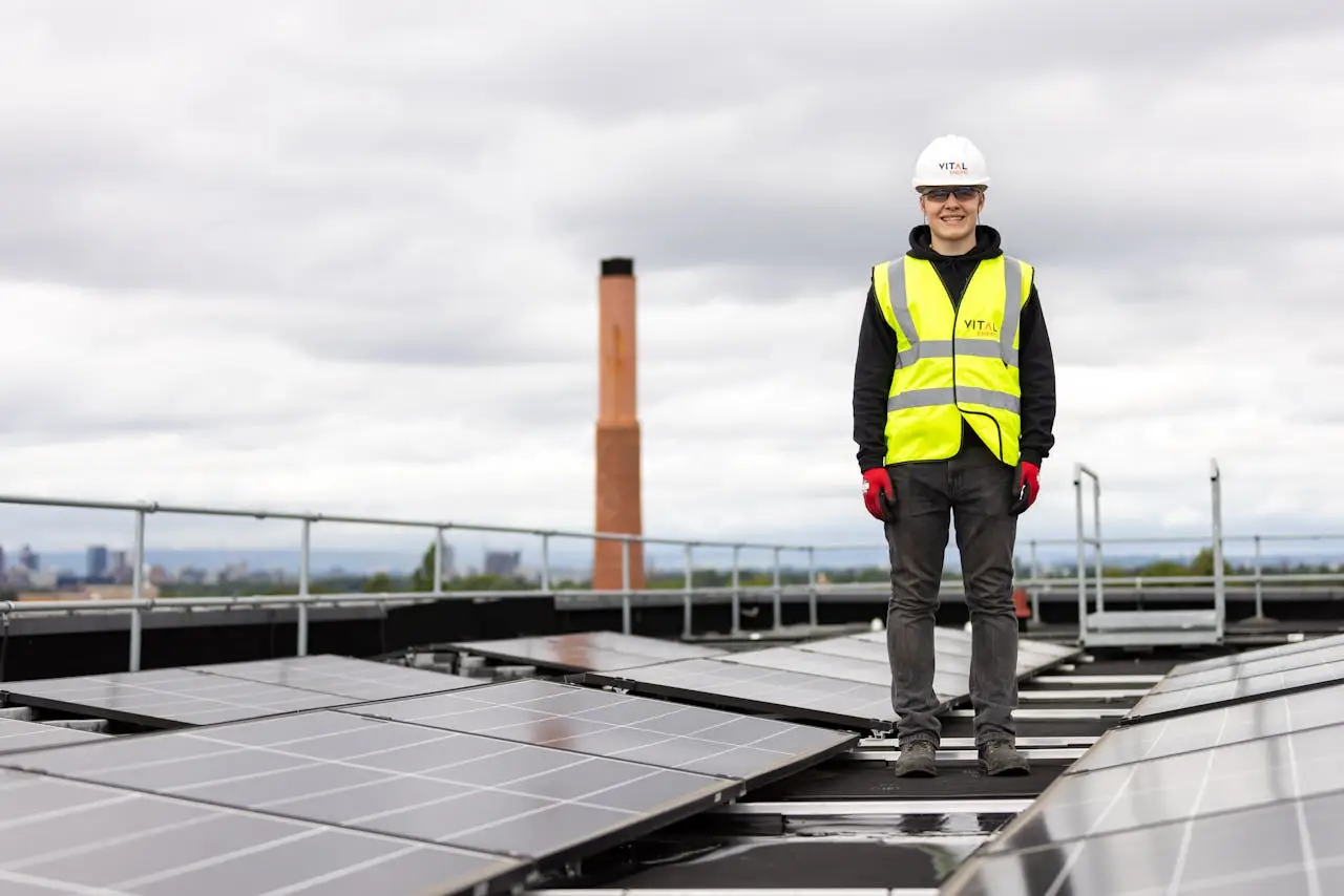 An engineer in a hard hat and safety vest inspects solar panels on a rooftop.