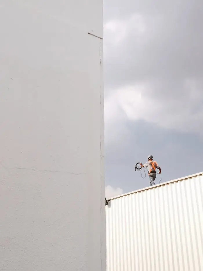 A construction worker stands on a rooftop against a large white wall, highlighting a minimalist aesthetic.