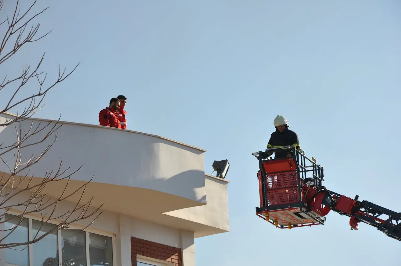 Firefighter on crane performing rescue on urban building rooftop under clear skies.
